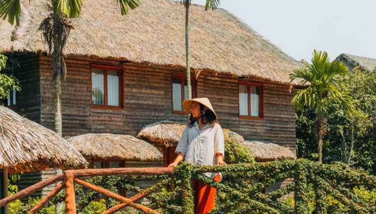 Una guida completa su cosa vedere in Vietnam: la blogger Elena Errante indossa il tipico cappello a cono davanti a un eco-lodge tradizionale in legno e paglia